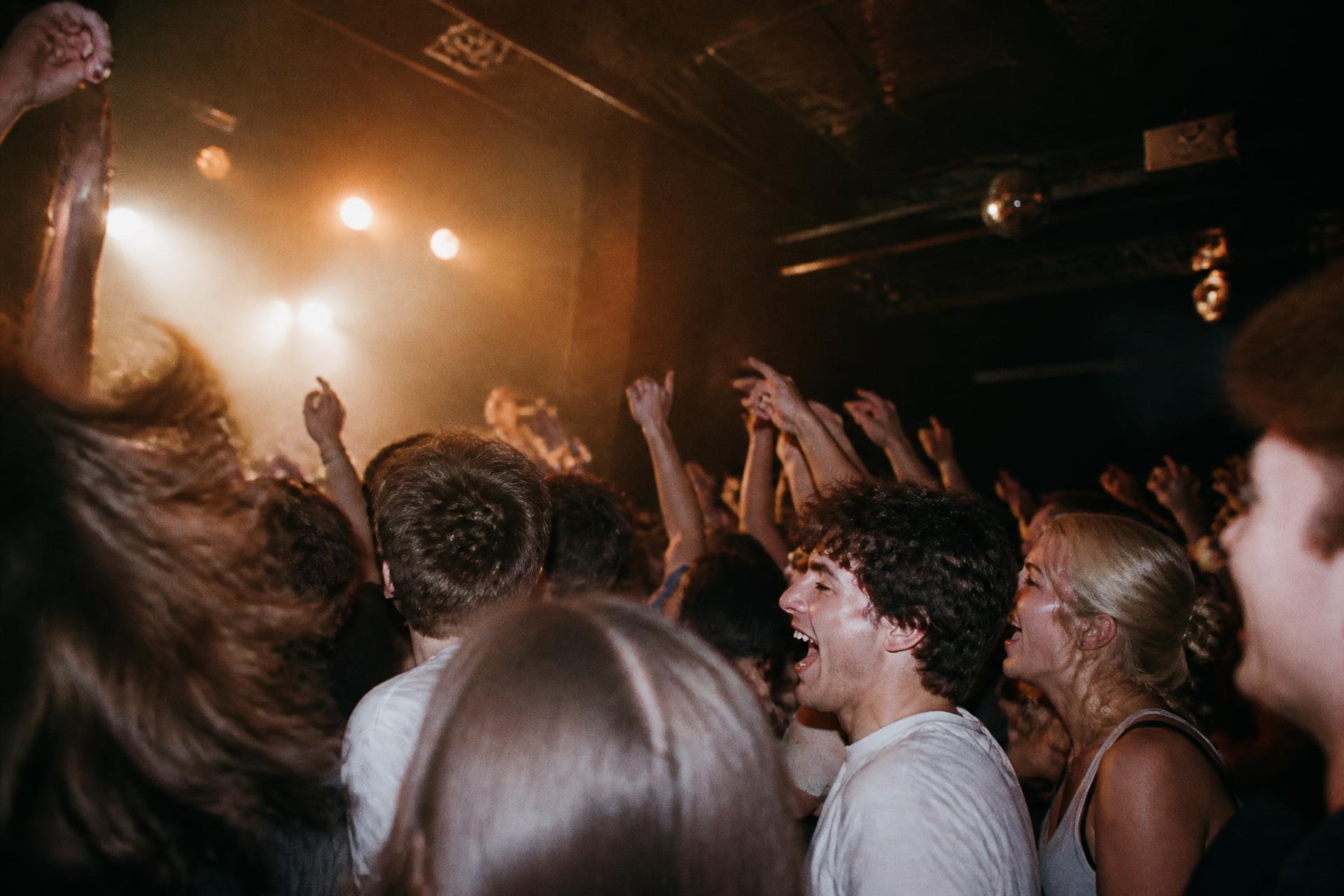 A concert crowd with hands in the air under warm stage lights