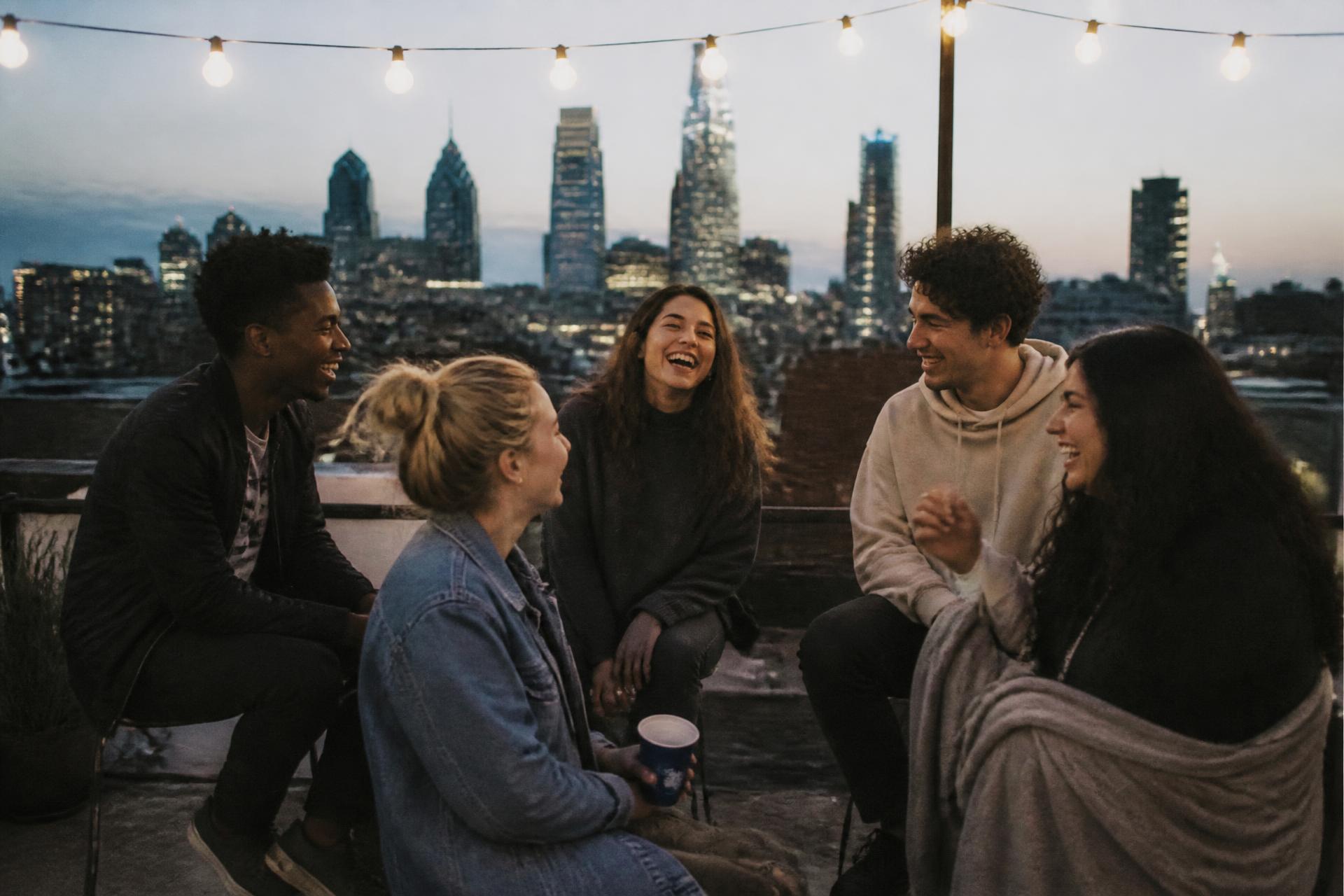 A group of five friends laughing together on a city rooftop at dusk