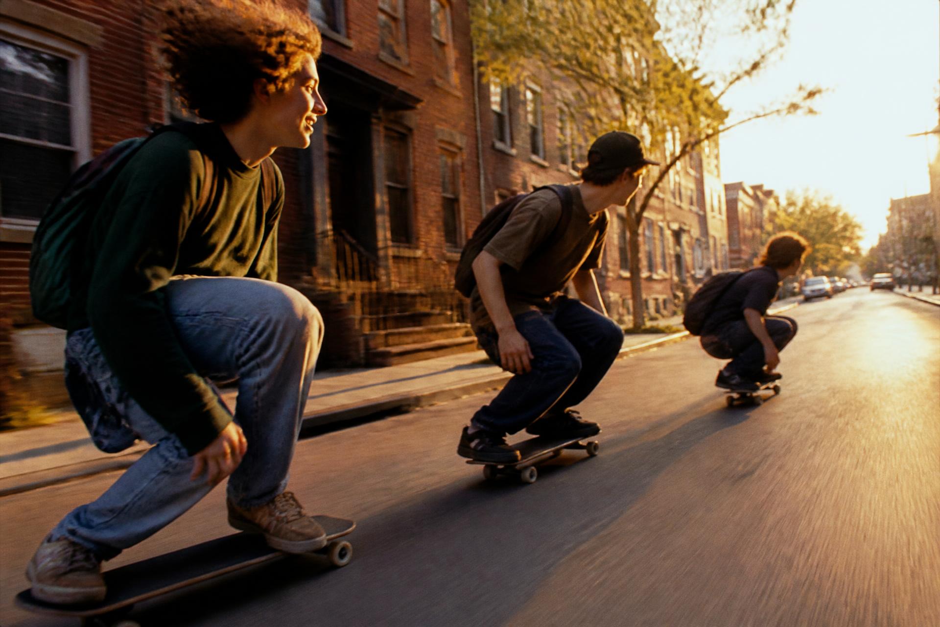 Three friends skateboarding down a Philadelphia rowhouse street at golden hour